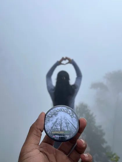 A creative shot of our Kodaikanal badge with a trekker making a heart shape in the misty background.