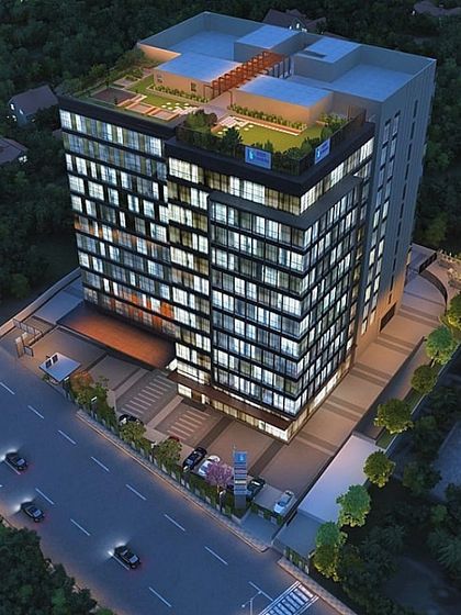 An aerial night view render of a commercial office building on Sarjapur Road, showcasing the rooftop amenities and the building's visibility from the street.