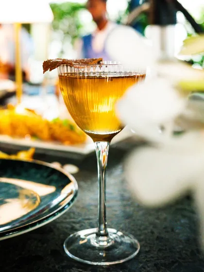A classic cocktail captured in a restaurant setting. The blurred background gives a sense of the ambiance while keeping the focus on the beautifully lit drink.