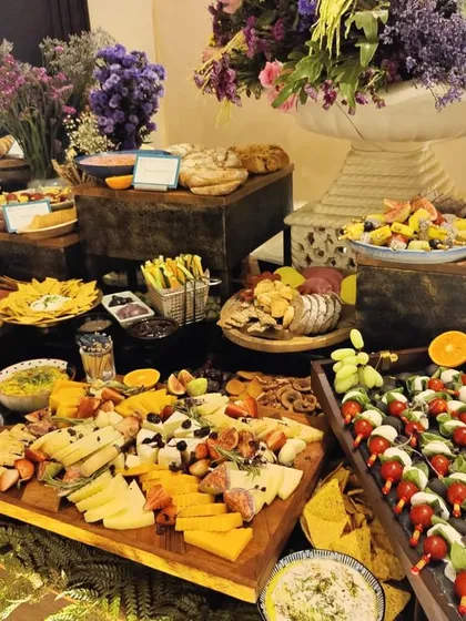 A beautiful grazing table designed for a special birthday celebration. The spread includes caprese skewers, various cheeses, dips, and breads, all surrounded by gorgeous floral arrangements.