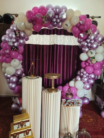 This full ring balloon arch in shades of purple, magenta, and white creates a rich and festive backdrop. The setup is completed with fluted pedestals for the cake and other decorative items.