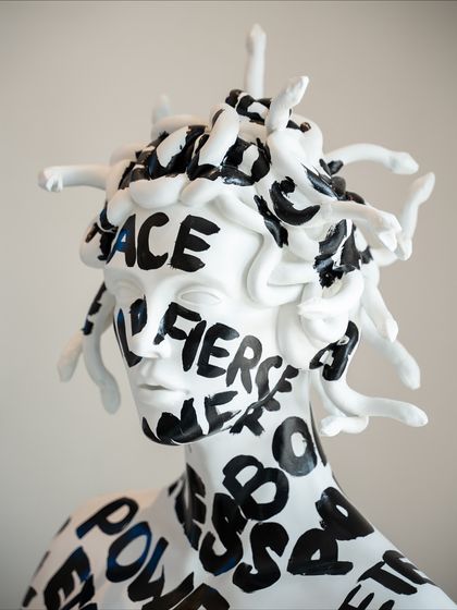 A close-up of Medusa's face, where words like "Fierce" and "Grace" are written across her features, redefining her story.