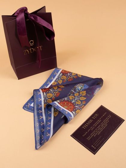 A folded pocket square with intricate floral patterns, shown with its branded gift bag and thank you card.