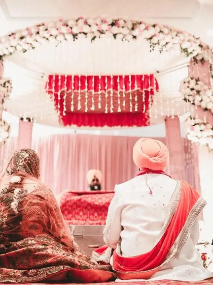 A serene moment from a Sikh wedding, showing the couple during the Anand Karaj ceremony from a respectful distance, with the beautiful mandap in the background.