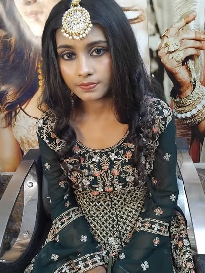 A party look featuring a dark green sharara suit. The makeup is focused on the eyes, with a maang tikka as a statement accessory.