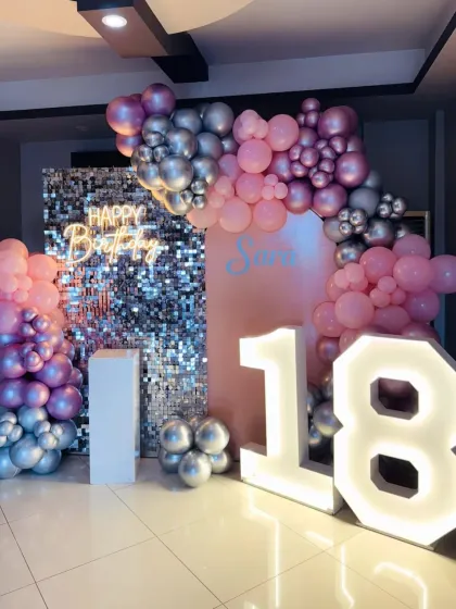 A stylish 18th birthday with a pink and silver balloon arch, a sequin wall, and large marquee numbers.
