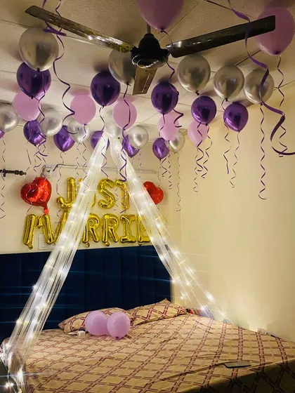 I specialize in first night room decorations to start your journey together beautifully. This setup includes "Just Married" foil balloons, a romantic canopy with fairy lights, and a stylish purple, pink, and silver balloon theme.