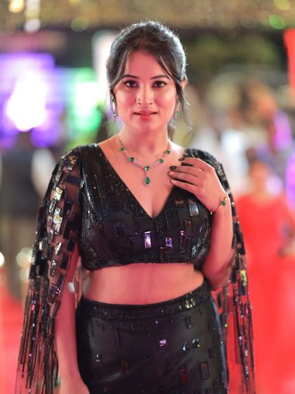 Anusha Rai posing with her hand on her neck, drawing attention to her elegant jewelry.