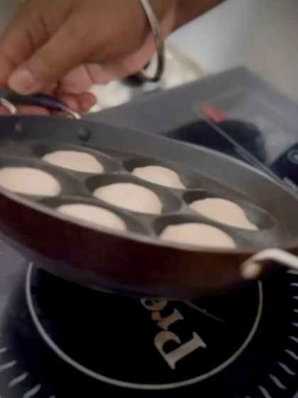 A chef holds a traditional paniyaram pan over the heat, demonstrating the live cooking process. This action shot emphasizes the freshness and authenticity of our South Indian food stations.