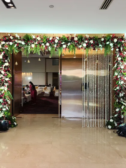 A lush floral arch created with red and white flowers, framing the entrance to the banquet hall. A curtain of crystal beads adds a touch of sparkle to the design.