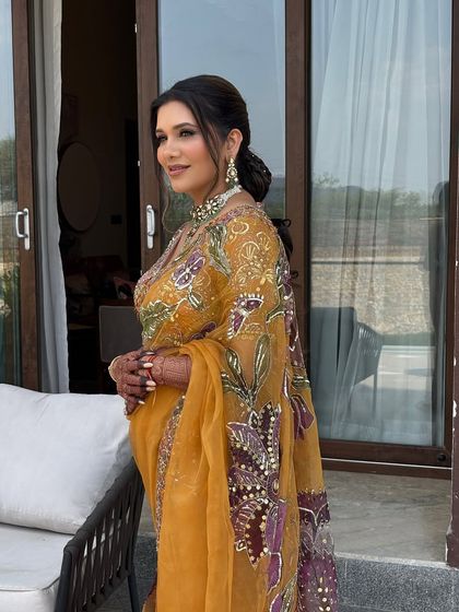 A beautiful braided ponytail on a client wearing a stunning yellow saree. The hair is braided at the top and flows into a messy, textured ponytail, creating a look that is both traditional and modern.