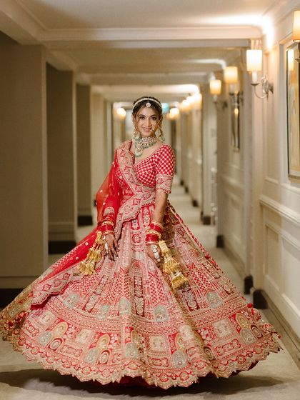The bride twirls in a grand hotel corridor, her magnificent red lehenga spreading out around her. A portrait of pure joy and bridal splendor.