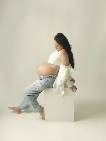 A profile view showcasing the gorgeous curve of the baby bump. The modern styling with jeans and a crop top is a confident celebration of the pregnant form.