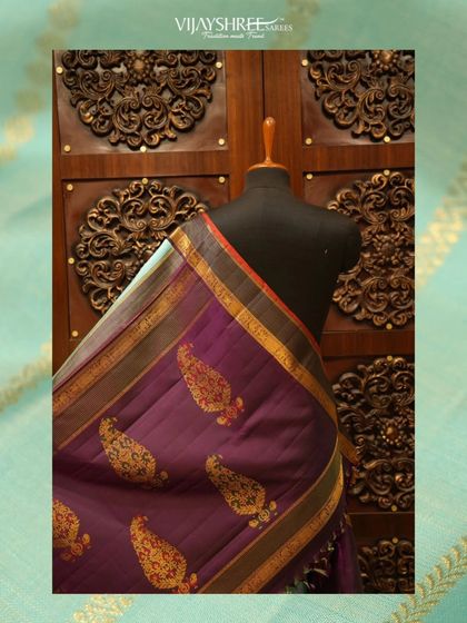 A deep purple Kanjivaram with large paisley buttas, set against a beautifully carved wooden backdrop.