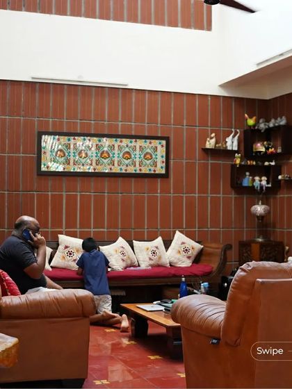 The cozy living room of the Manjunath Residence, with warm leather sofas and a terracotta brick accent wall, creating a comfortable and earthy atmosphere.