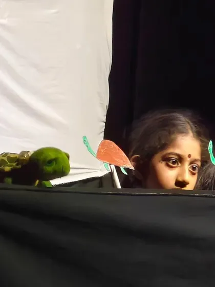 A close up of a young girl during a puppet show, her eyes wide with wonder as she brings her character to life.