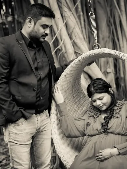 A quiet, romantic moment captured in black and white. The dad-to-be looks lovingly at his partner as she rests in a hanging chair.
