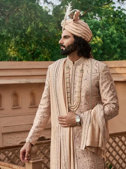 For the modern groom who honors tradition, I present this regal sherwani in a subtle pastel hue. The complete ensemble, from the feathered safa to the layered pearl necklace and the intricately embroidered stole, is designed to create a timeless and majestic wedding day look.