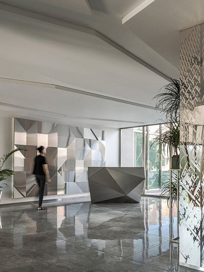 The reception area on one of the office floors at the Stainless Steel Office. The faceted desk and wall panels are a recurring motif, reinforcing the company's focus on steel fabrication and design.
