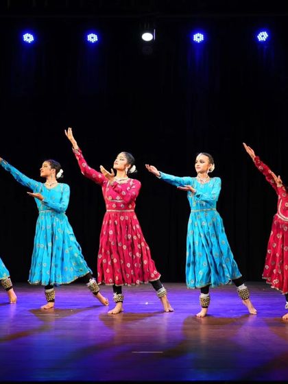The full line of Sāttvatī dancers on stage, their arms extended in a graceful pose that captures the expansive nature of our group performances.