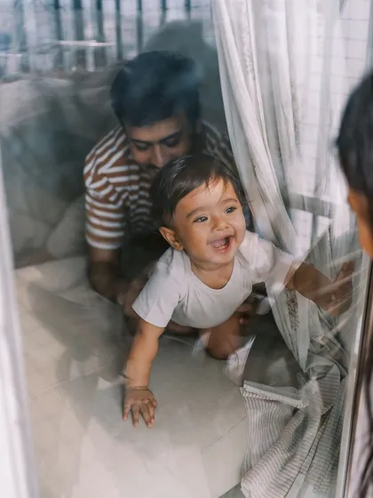 A candid shot of a nine-month-old playing peek-a-boo through a window, full of laughter and fun.