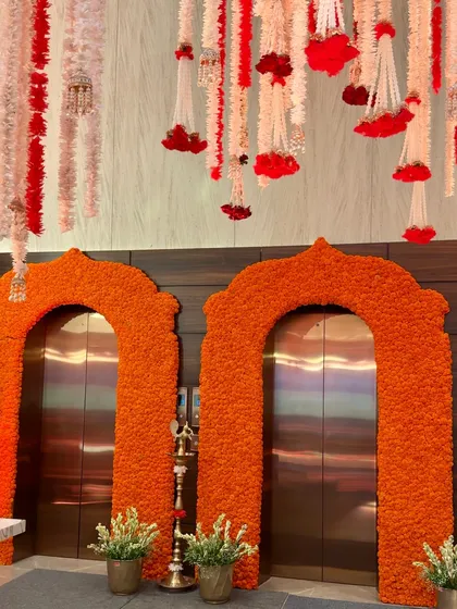 The marigold arches are complemented by hanging red and white floral strings from the ceiling, adding another layer of festive color and detail.