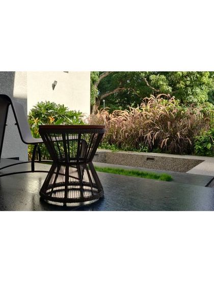 A quiet corner of a patio with a comfortable chair and table, looking out onto a bed of ornamental grasses. This space is designed as a personal retreat for enjoying the peace and beauty of the garden.