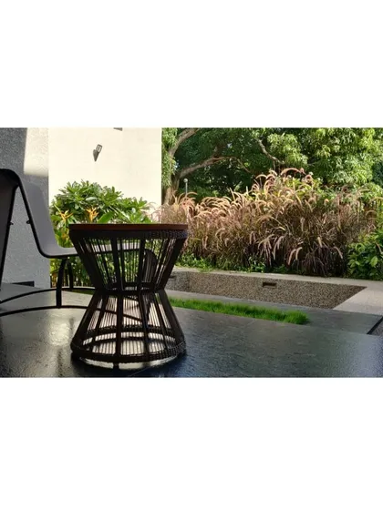 A quiet corner of a patio with a comfortable chair and table, looking out onto a bed of ornamental grasses. This space is designed as a personal retreat for enjoying the peace and beauty of the garden.