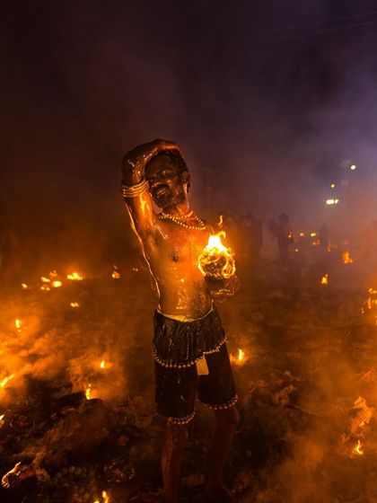 Surrounded by a field of fire, a devotee stands in a moment of ecstatic trance, his body illuminated by the countless small blazes of the ritual.