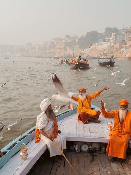 A wide shot of three sadhus enjoying a boat ride on the Ganga, surrounded by birds and the city's ghats in the background. It’s a perfect summary of a classic Varanasi morning.