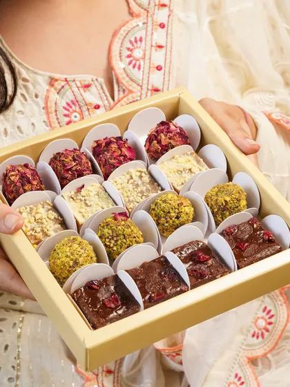 A box of assorted vegan mithai, including pistachio and rose-covered ladoos, held as a perfect gift for the festive season.