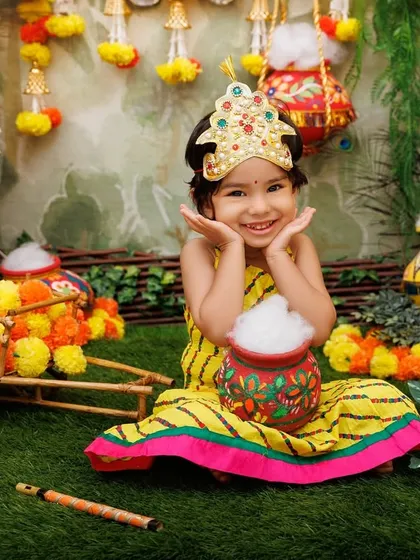 This little Radha's adorable expression, with her hands framing her face, makes for a truly memorable and cute portrait.