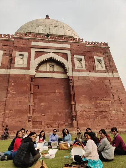 A moment of rest and reflection for the group in front of Ghiyasuddin Tughluq's tomb. This fortified mausoleum, built of red sandstone and white marble, is a starkly beautiful example of early Sultanate architecture.