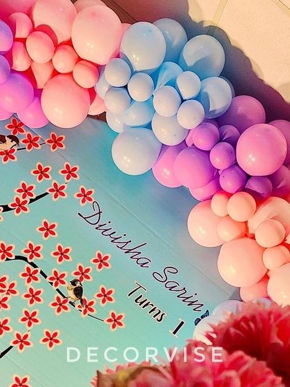 A detailed shot of the custom backdrop for Divisha's party. The cherry blossom print and personalized name are framed by a beautiful pastel balloon garland.