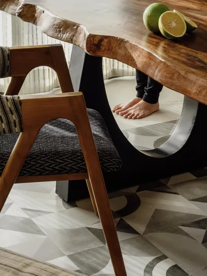 A close-up look at the junction of the live-edge dining table and a custom dining chair. You can see the texture of the wood, the geometric pattern on the floor, and the clean lines of the chair's upholstery. The small details are what make a project complete.