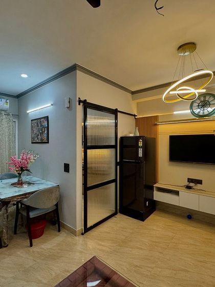 This image shows the full living and dining space, with the TV unit, dining table, and a stylish barn door partition for the kitchen.