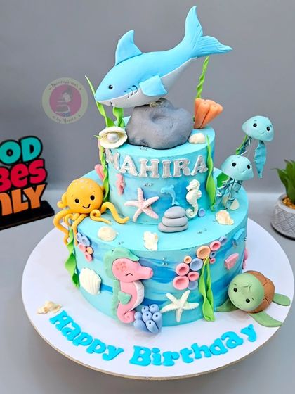 A vibrant two-tier underwater cake featuring a shark, octopus, seahorses, and a turtle.
