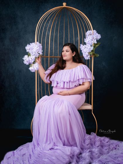 A queen on her throne. This mom-to-be looks majestic in a lavender gown, seated in our golden birdcage prop adorned with matching flowers.