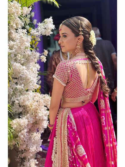 A beautiful shot of the bride's look from the back. The focus is on her intricate braid and the delicate details of her blouse and traditional bandhej dupatta.