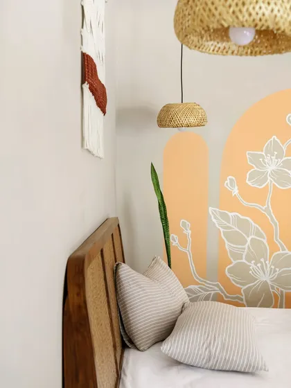 A close-up of the custom mural and woven pendant lamp in the bedroom. The soft peach tones and delicate floral line work add a touch of artistry and warmth to the otherwise neutral and calming space.