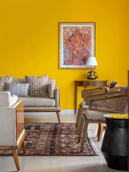 The 'Vasudhalayah' living room features a bold yellow accent wall, which serves as a vibrant backdrop for the ethnic-inspired furniture and decor.