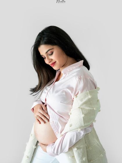 A serene portrait of a mom-to-be in a soft pink shirt, gently holding her baby bump.