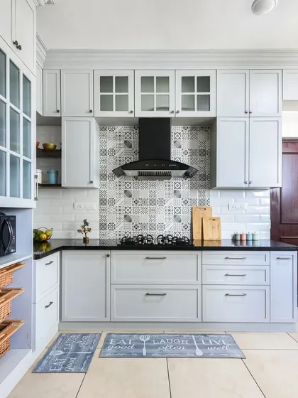 This classic kitchen features soft grey shaker cabinets, white subway tiles, and a patterned tile backsplash. Fluted glass on some of the upper cabinets adds a vintage touch.