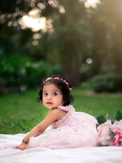 A dreamy outdoor portrait. The soft, golden light and lush green background create a magical atmosphere for this little girl's first birthday photos.