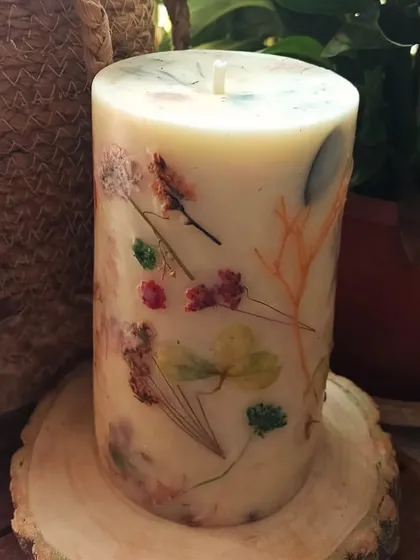 Our floral love pillar candle, resting on a rustic wooden slice. It's a beautiful blend of natural elements, perfect for creating a calming and aesthetic atmosphere.