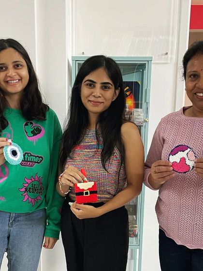 A group of ladies proudly displaying their finished pieces, including an evil eye, a Santa ornament, and a planet design.