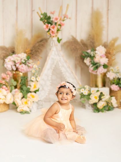 A beautiful, calm portrait before the cake smash fun begins. This little girl looks so sweet and happy in her peach dress against the floral and teepee backdrop.