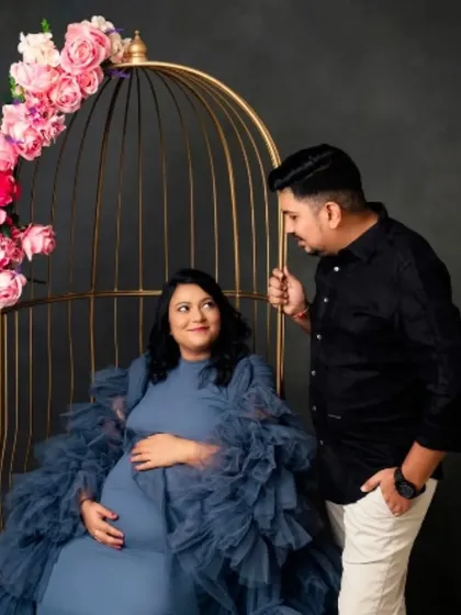 A whimsical couple's portrait with the mom-to-be in our blue ruffled gown, seated in a golden birdcage prop.