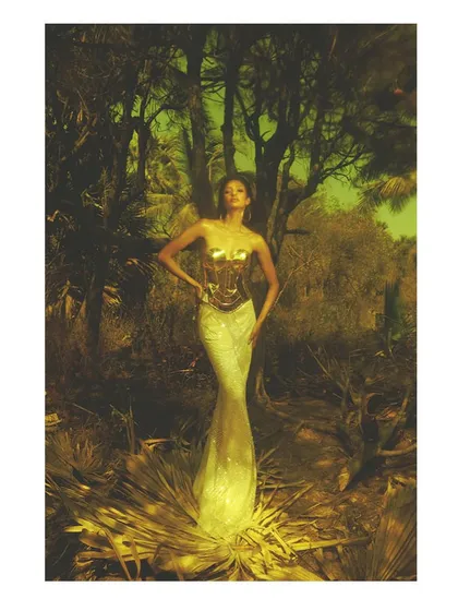 A portrait from the 'Emergence' series. The model is styled in a golden corseted gown, standing in a surreal, yellow-toned forest. This image blends studio techniques with a natural setting to create a fantasy world.