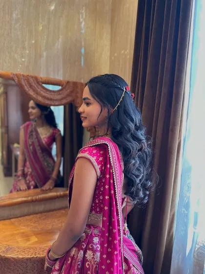 A beautiful half-updo with soft curls and a delicate floral hair vine. The client is admiring her look in the mirror.